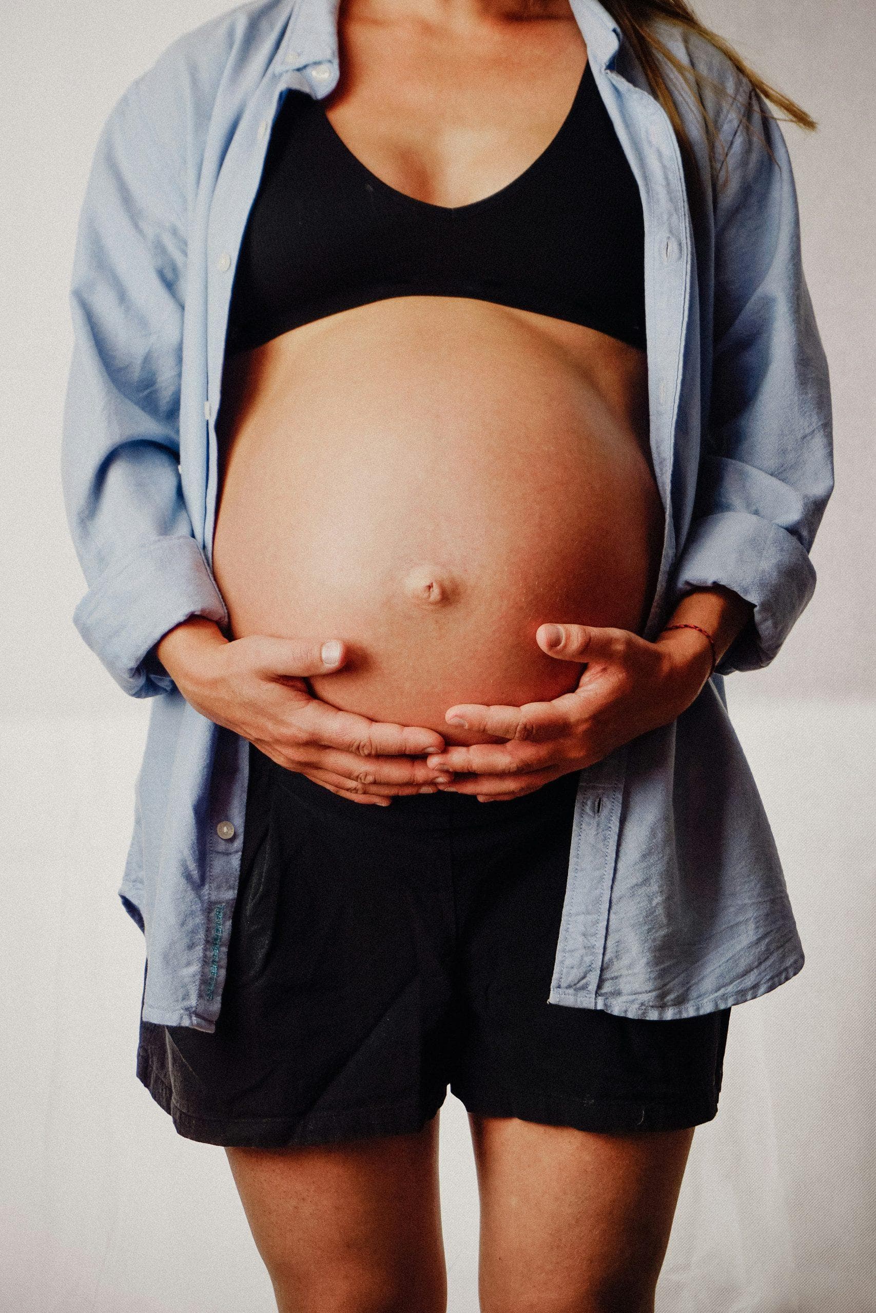 A pregnant belly in a blue shirt, hands resting on it