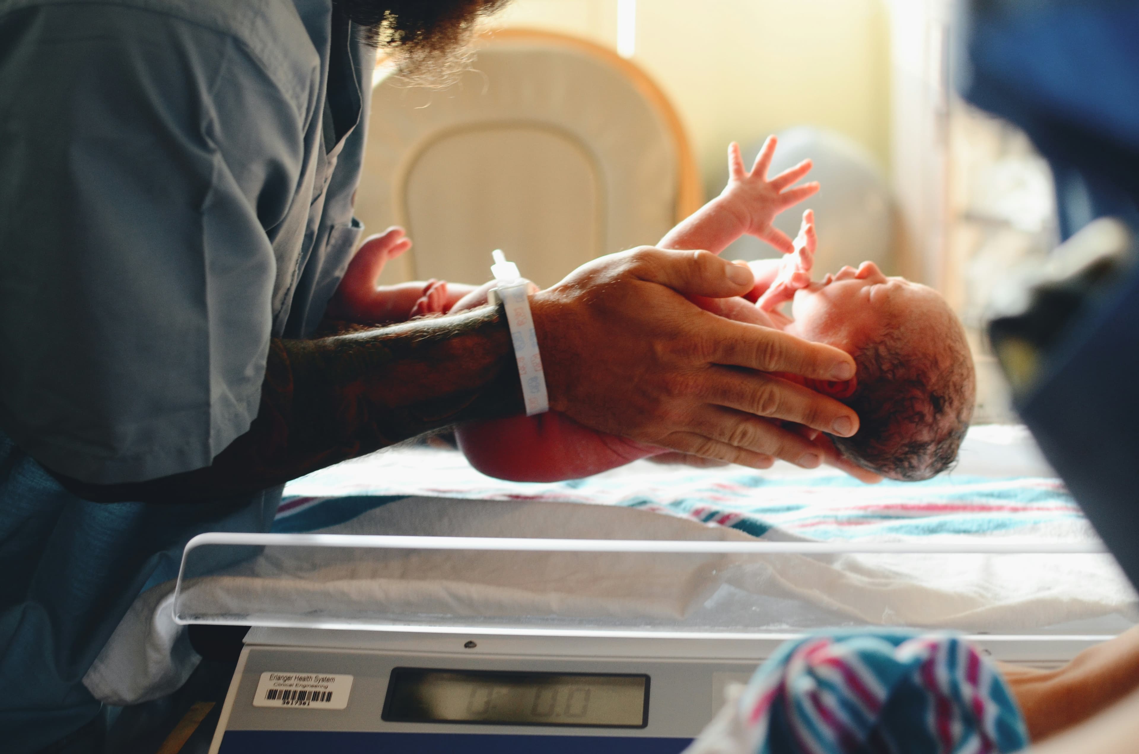 A newborn baby being weighed on a hospital scale in warm window light