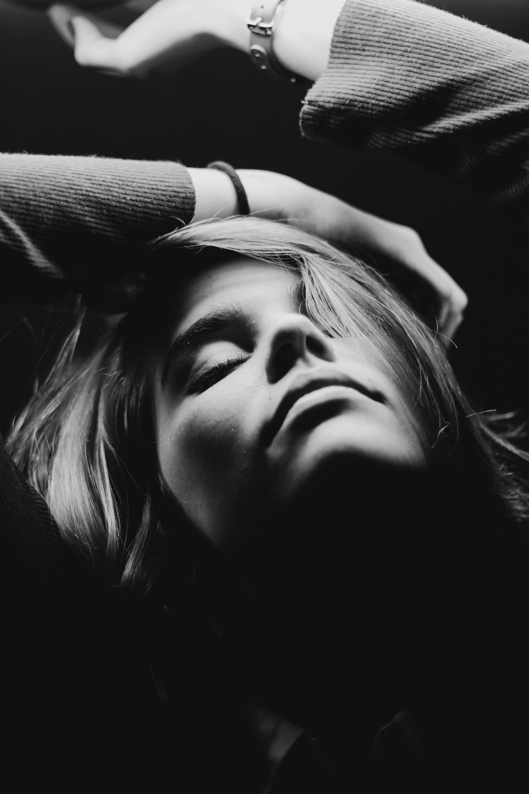 A woman lying down with her eyes closed, one arm resting above her head