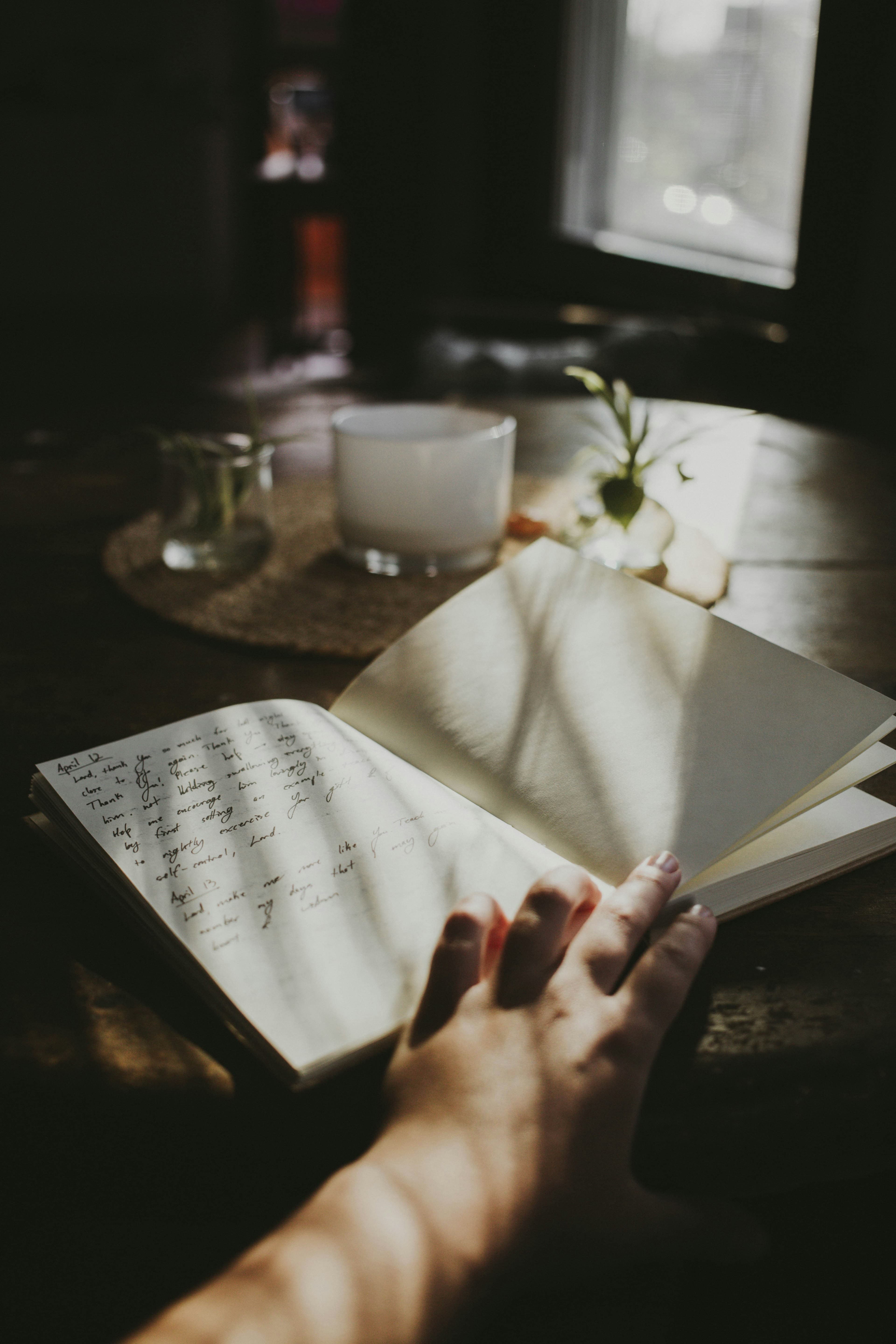 A hand resting on an open journal in soft window light, a candle nearby