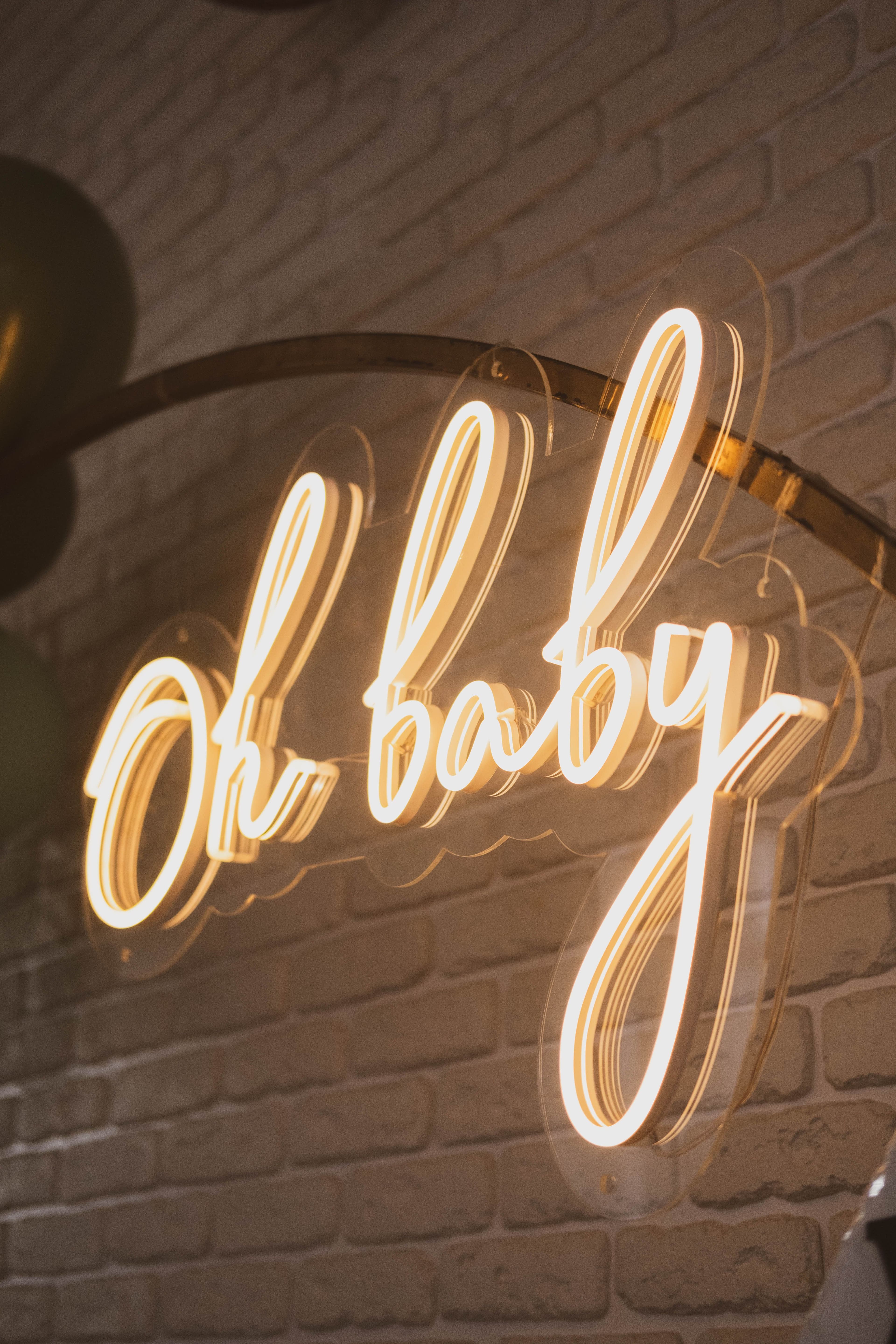 A glowing neon Oh baby sign on a white brick wall