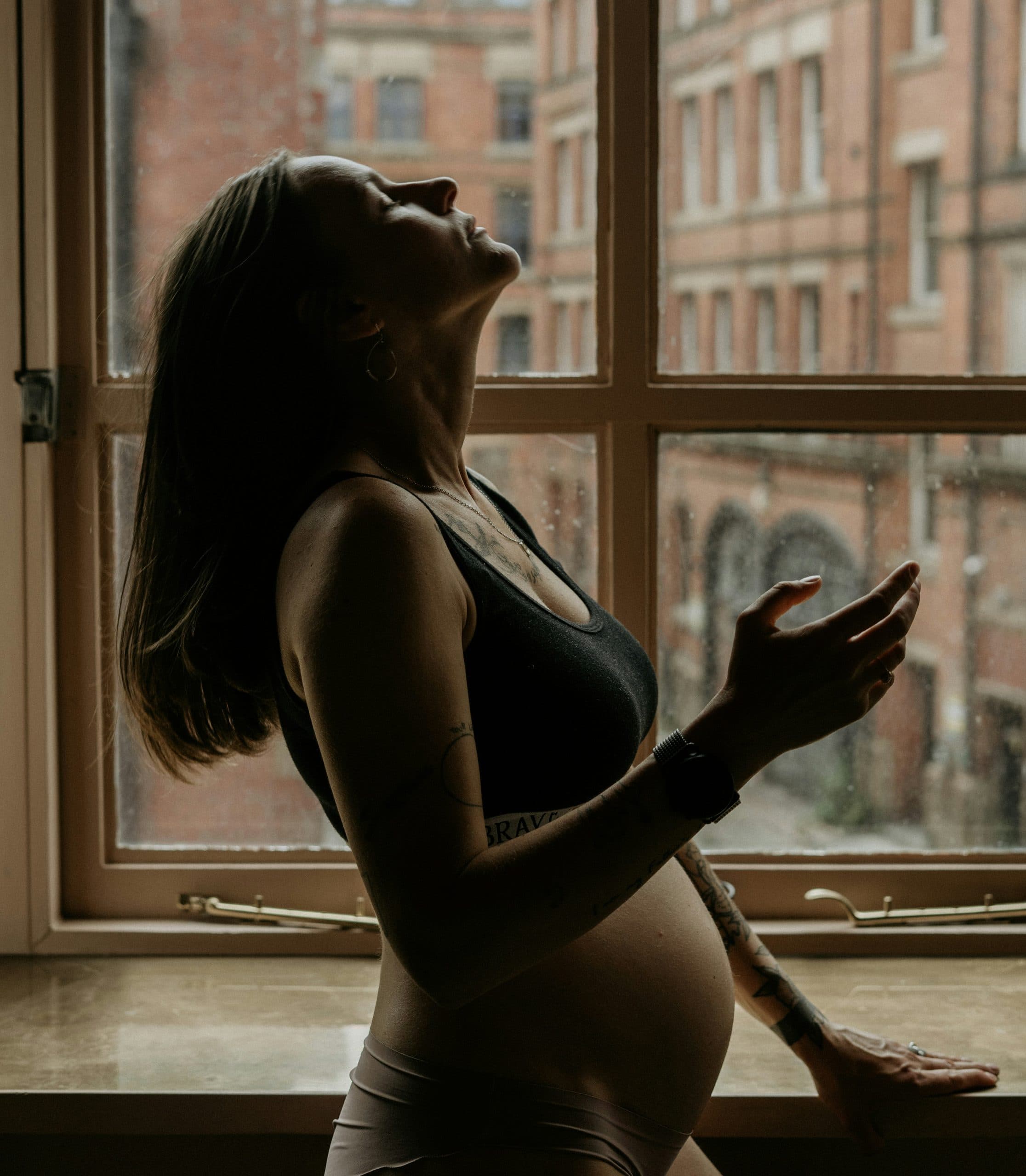 A pregnant woman standing in soft window light