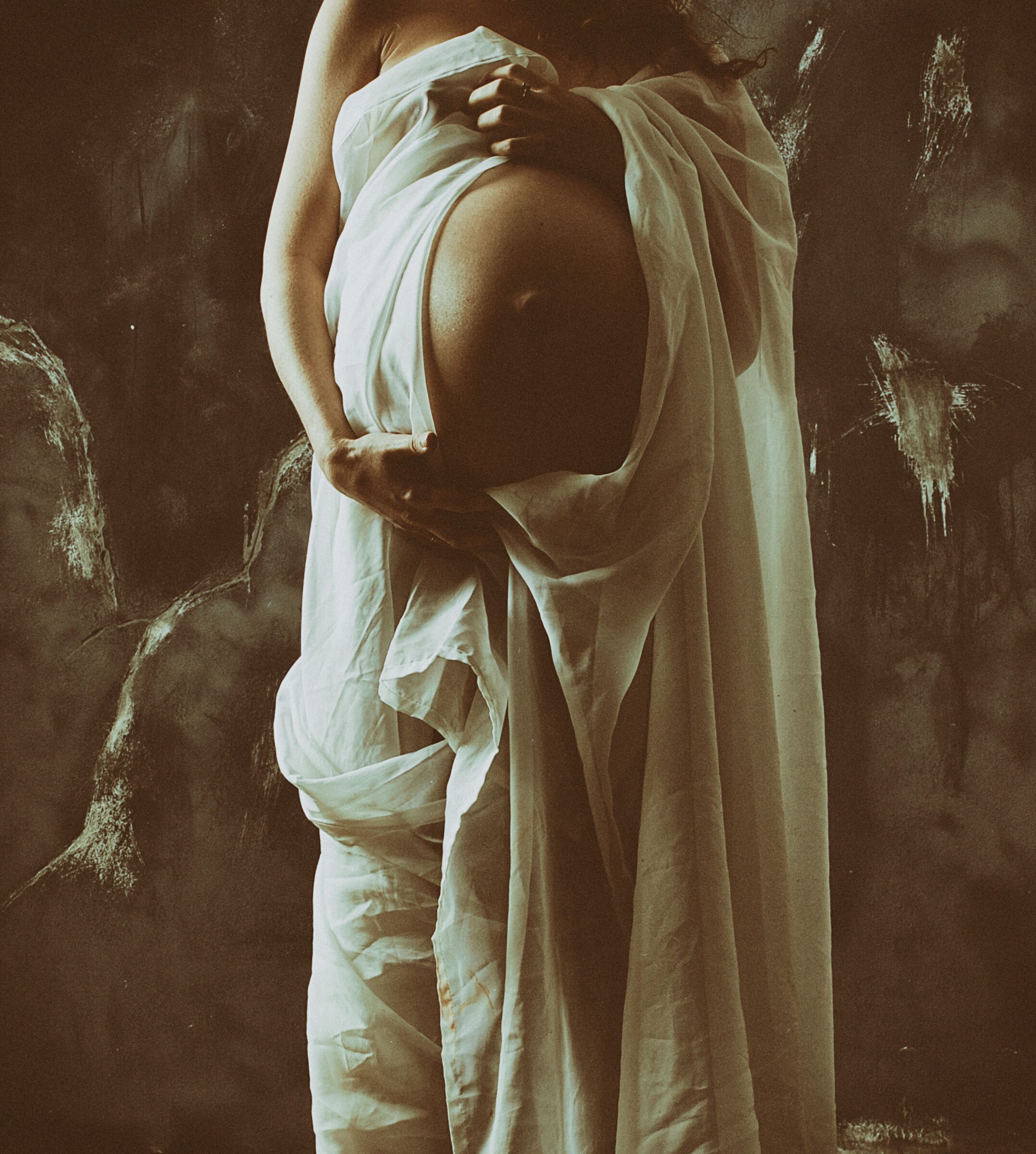 A pregnant woman cradling her belly, wrapped in soft cloth